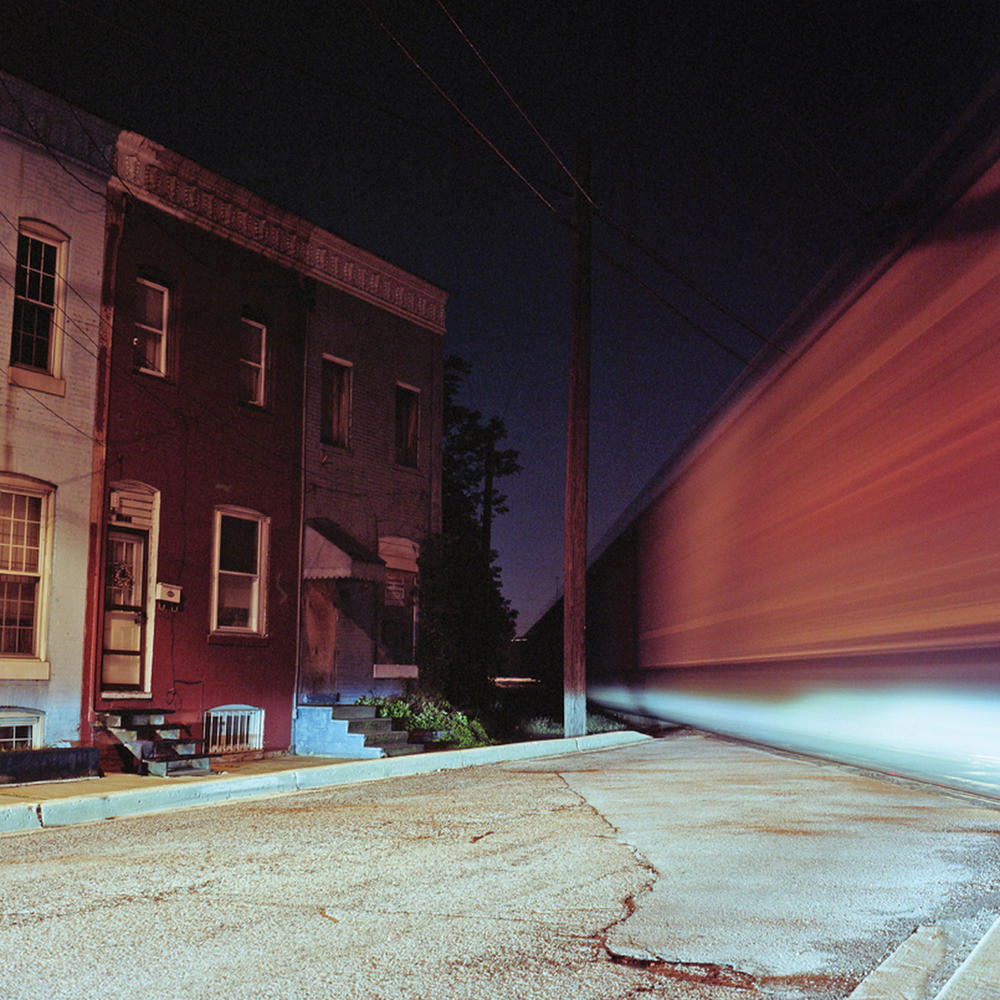 A freight train passes by row homes on the edge of Cherry Hill while the headlights of waiting cars shine through. –Photography by Patrick Joust